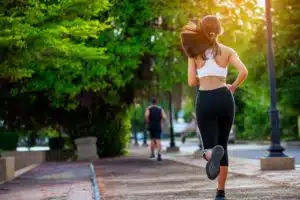 A woman is running on the sidewalk in her sports bra.